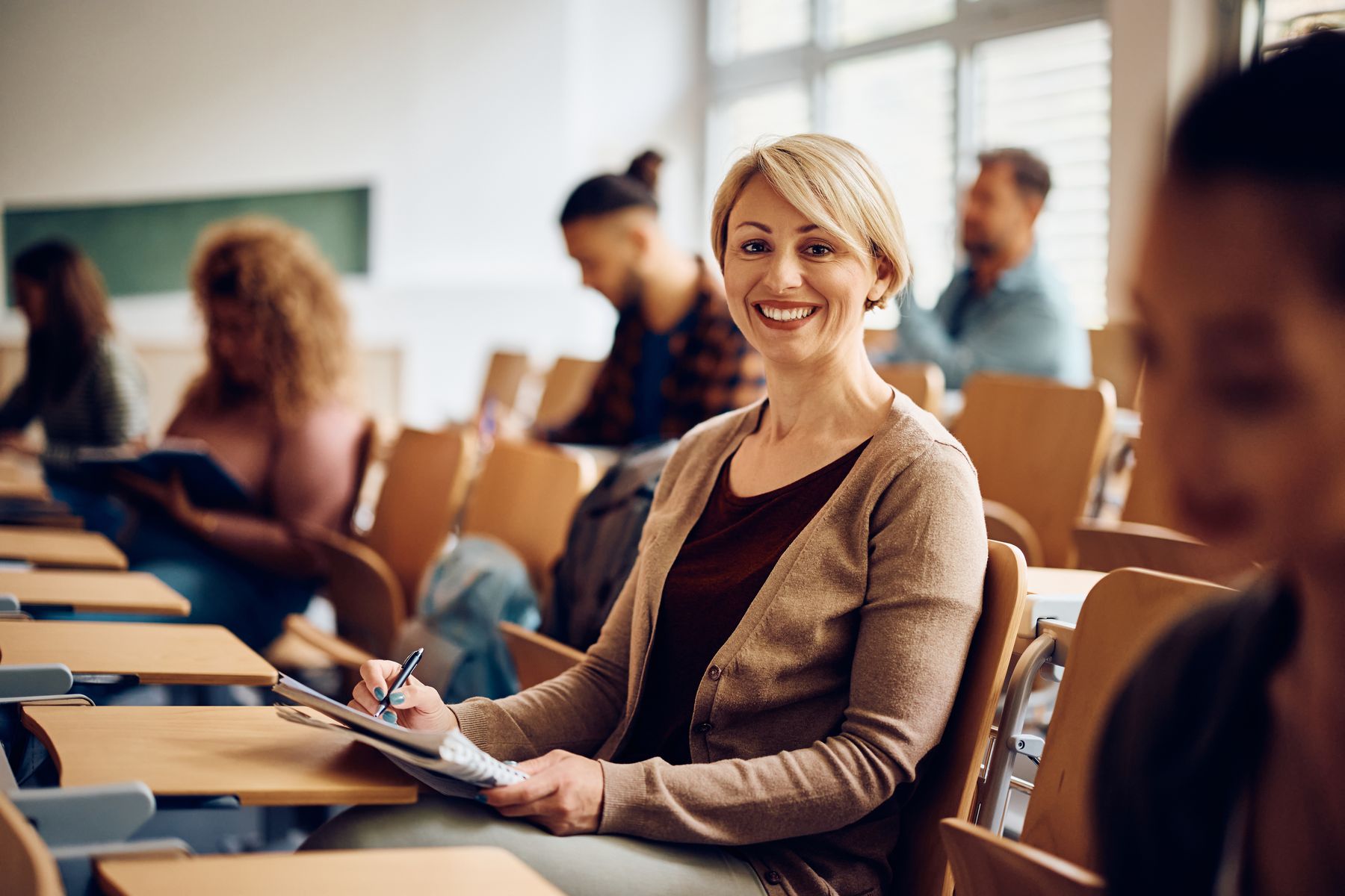 An adult learner smiling at her desk in a university classroom