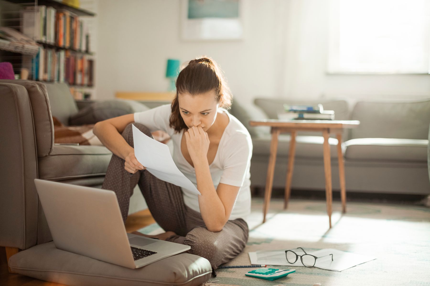 A student on her living room floor with a laptop, reading through papers