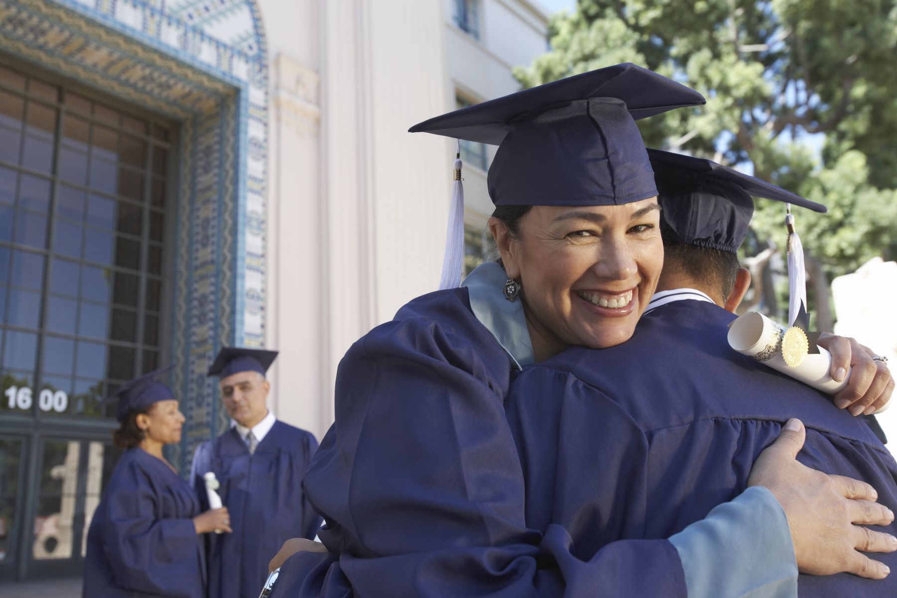 A smiling graduate in cap and gown hugging a classmate