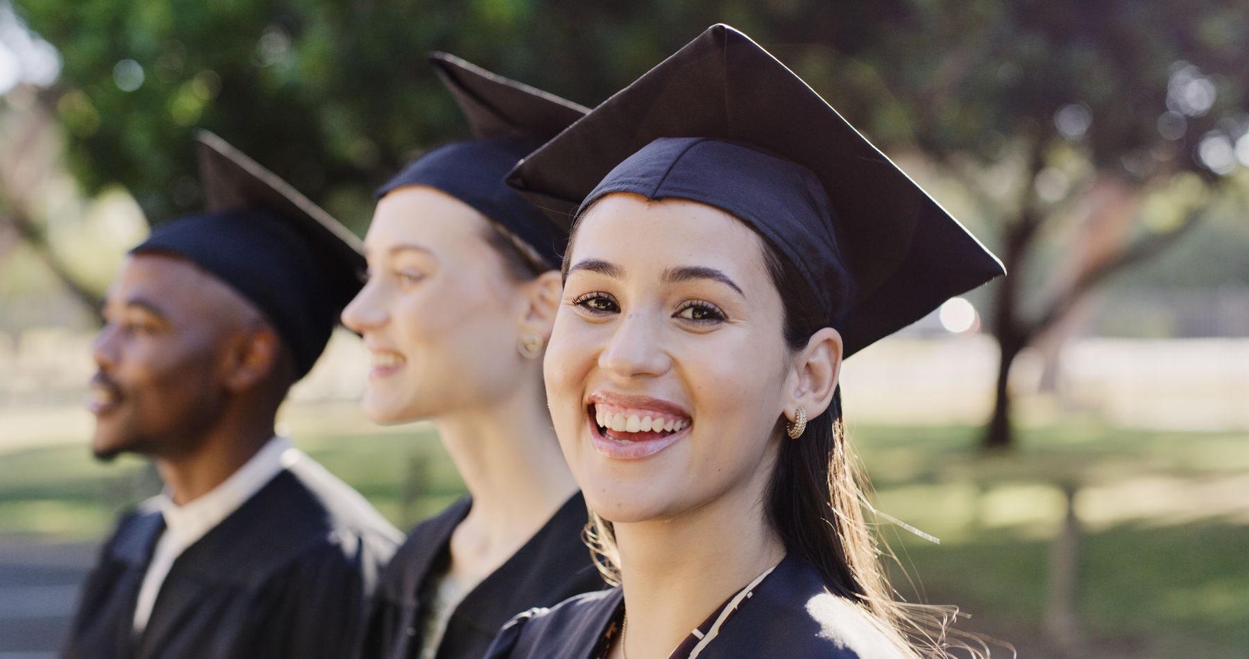 Three graduates in caps and gowns; one smiles at the camera