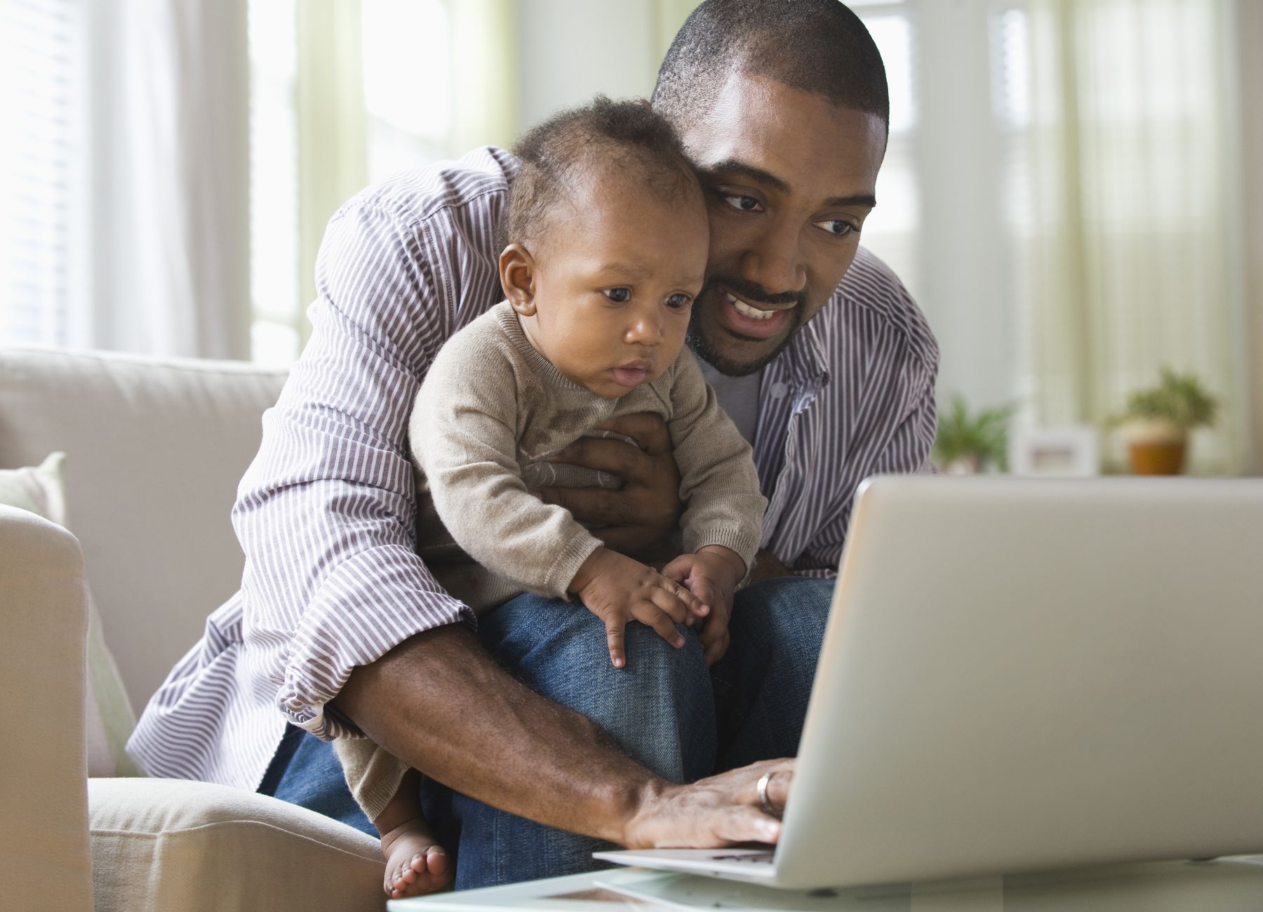 A father holding his baby while he works on a laptop at home